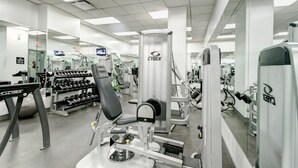 Et fitnessrum med forskellig træningsudstyr, herunder håndvægte, en bænkpres og en Cybex-maskine.