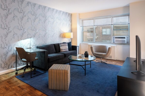 A modern living room with a sofa, armchair, ottoman, glass coffee table, and a flat-screen TV.