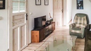 A living room with a glass coffee table, a television on a wooden stand, a plaid armchair, and a door leading to another room. - Beautiful apartment in Wolin (Wolin)