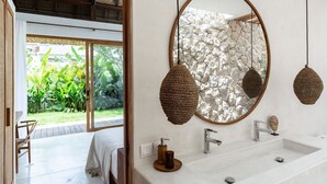A modern bathroom with a large mirror, two sinks, and a stone wall. - Las Lunas Villas Canggu (Canggu)