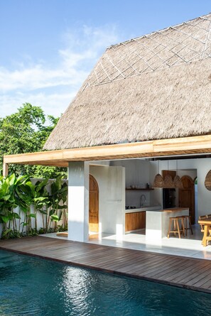 A modern house with a thatched roof, a pool, and a wooden deck. - Las Lunas Villas Canggu (Canggu)