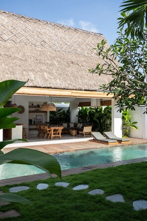 A poolside area with a thatched roof, wooden furniture, and lush greenery. - Las Lunas Villas Canggu (Canggu)
