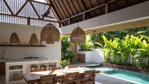 A modern outdoor kitchen with a dining area, a pool, and lush greenery. - Las Lunas Villas Canggu (Canggu)
