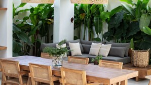 A dining area with a wooden table and chairs, a sofa, and hanging rattan lamps. - Las Lunas Villas Canggu (Canggu)
