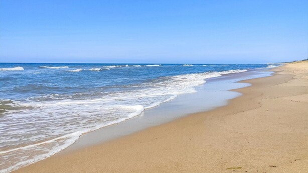 Ein Strand mit klarem, blauem Wasser und sandigem Ufer.