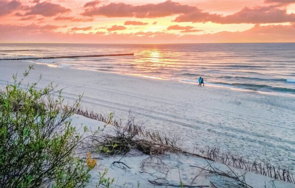 Une plage au coucher du soleil, avec une mer calme et une personne qui se promène.