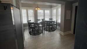 Un espace repas comprenant une table ronde et des chaises, un lustre et de grandes fenêtres.