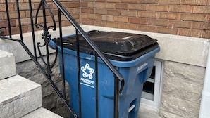 Une poubelle de recyclage bleue, ornée du symbole du recyclage et portant l’inscription « Republic Services », est placée à côté d’un bâtiment en briques doté d’une fenêtre et d’un escalier en métal noir.