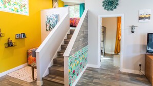 Una escalera con un diseño artístico y colorido en la pared, una estantería con libros, y un elemento decorativo en la pared.