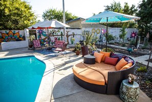 A poolside area with a curved wicker sofa, a chair, and a small table with a decorative vase.