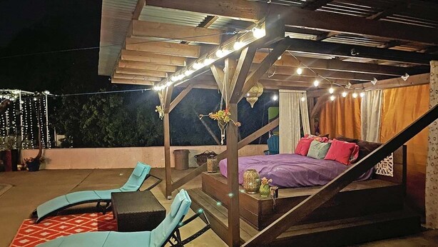 Un patio exterior con sillones de descanso, una mesita y una cama con ropa de cama colorida.