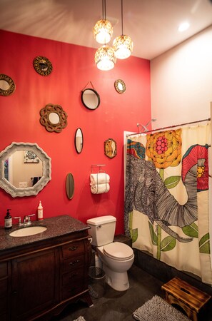 A bathroom with a red wall, a white toilet, a wooden vanity, and a shower curtain with a floral design.