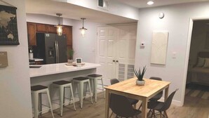 Uma cozinha moderna com ilha central, banquetas e uma mesa de jantar com cadeiras.