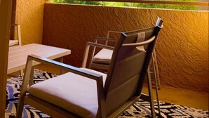 Uma varanda com vista para um prédio, corrimão e uma mesa com cadeiras.