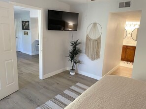 A room with a bed, a TV mounted on the wall, a macrame wall hanging, and a potted plant. - Mountain view Hideaway w/3 Pools (Scottsdale)
