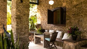 Un patio con paredes de piedra, una mesa de vidrio, sillas y un banco.
