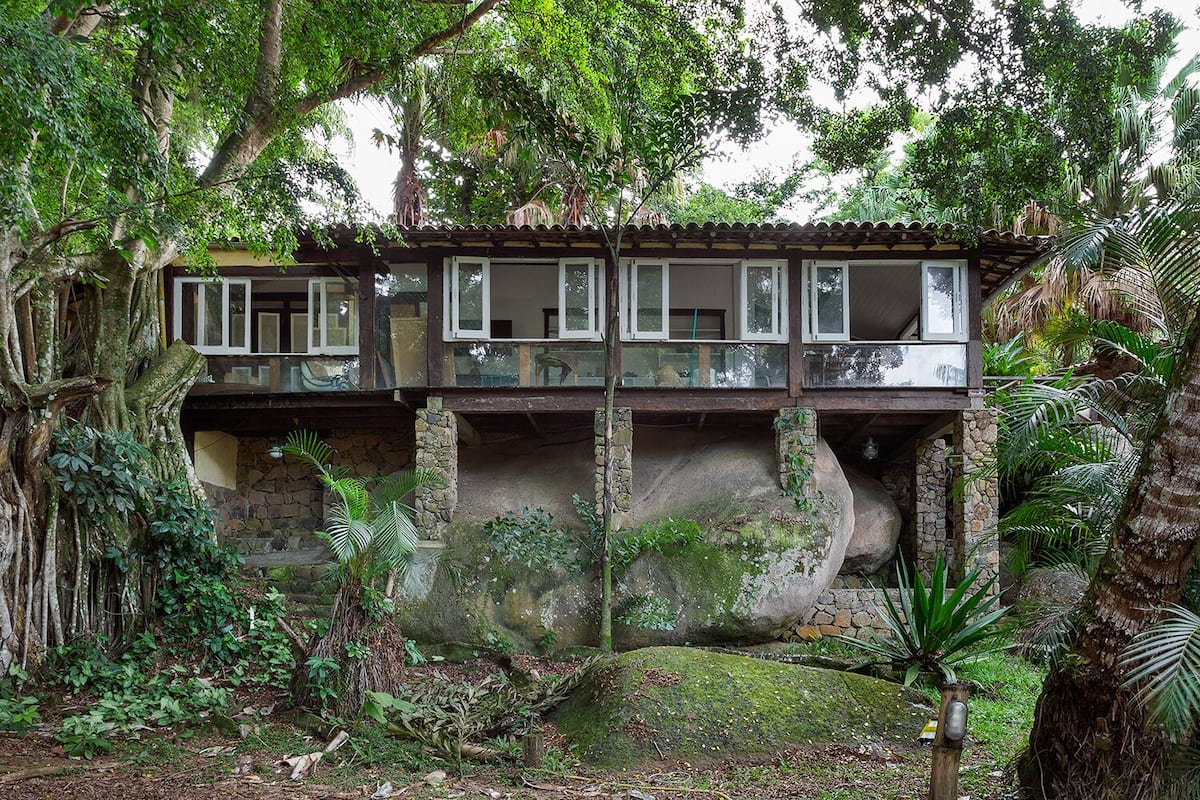 Een twee verdiepingen tellend huis met een balkon, omgeven door weelderige begroeiing en bomen.
