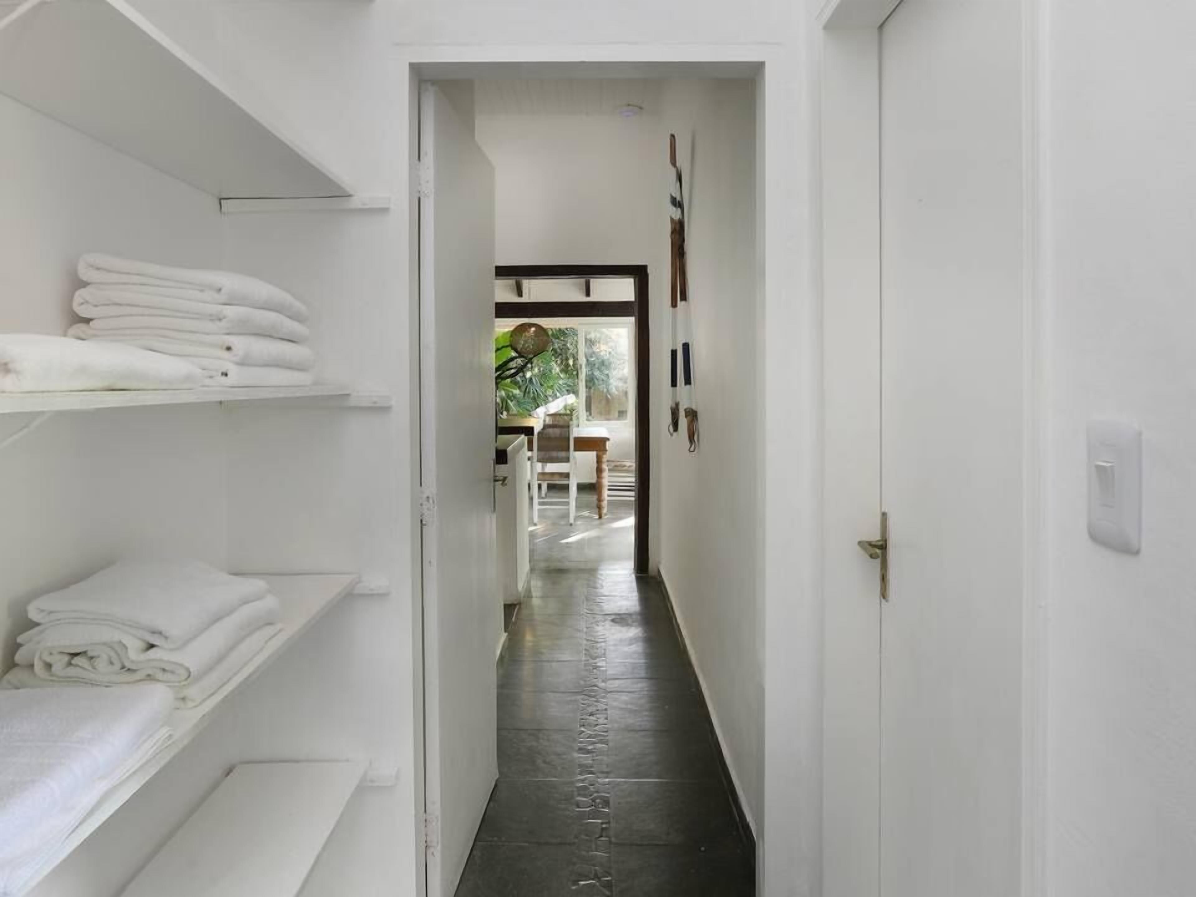 A narrow hallway with white walls and a tiled floor leading to a dining area.