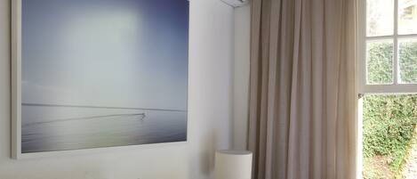 A neatly made bed with white bedding, a bedside lamp, and a large painting of a beach scene on the wall.