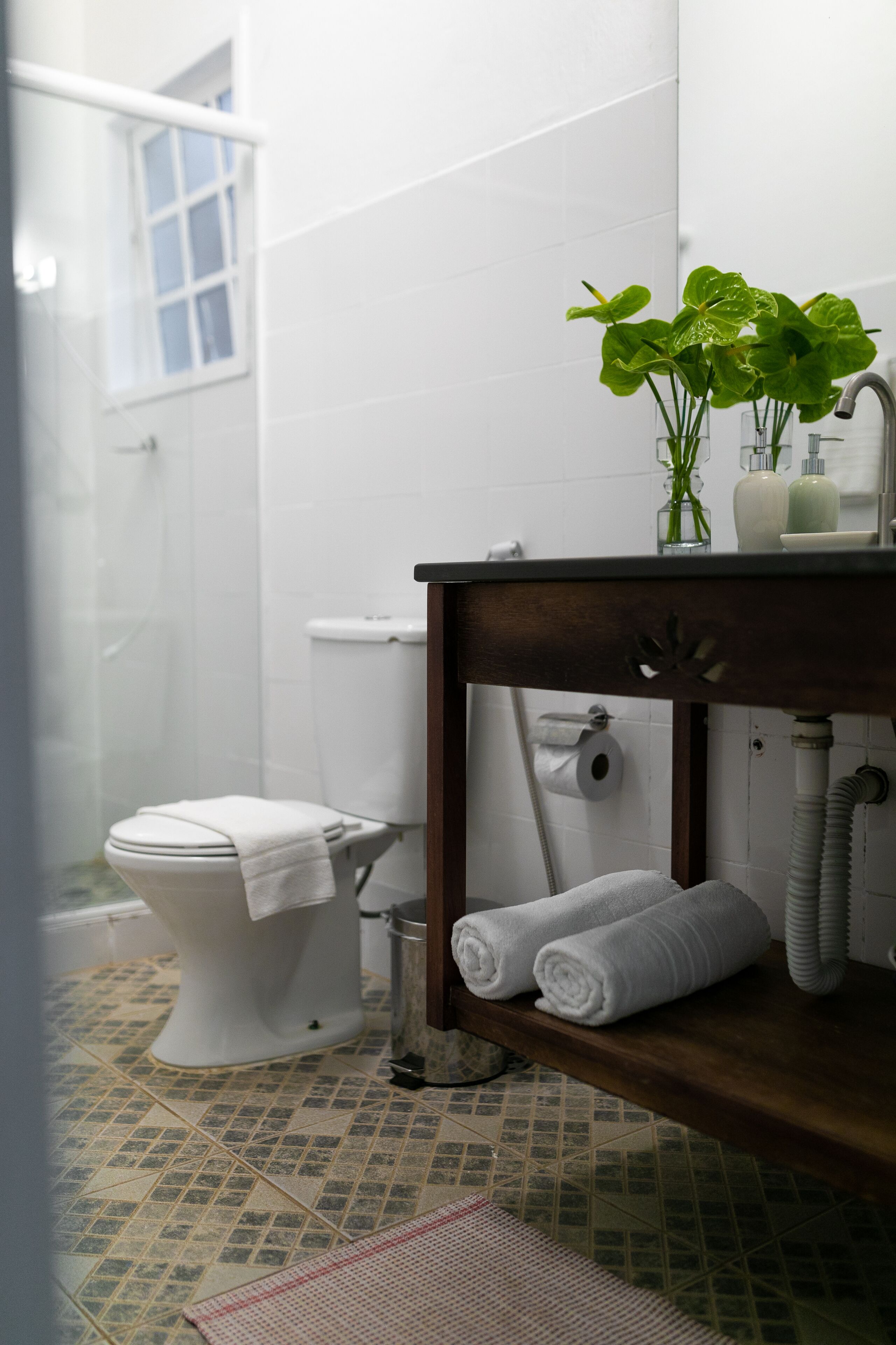 A bathroom with a toilet, a sink, and a shower. There are towels on the floor and a plant on the sink.