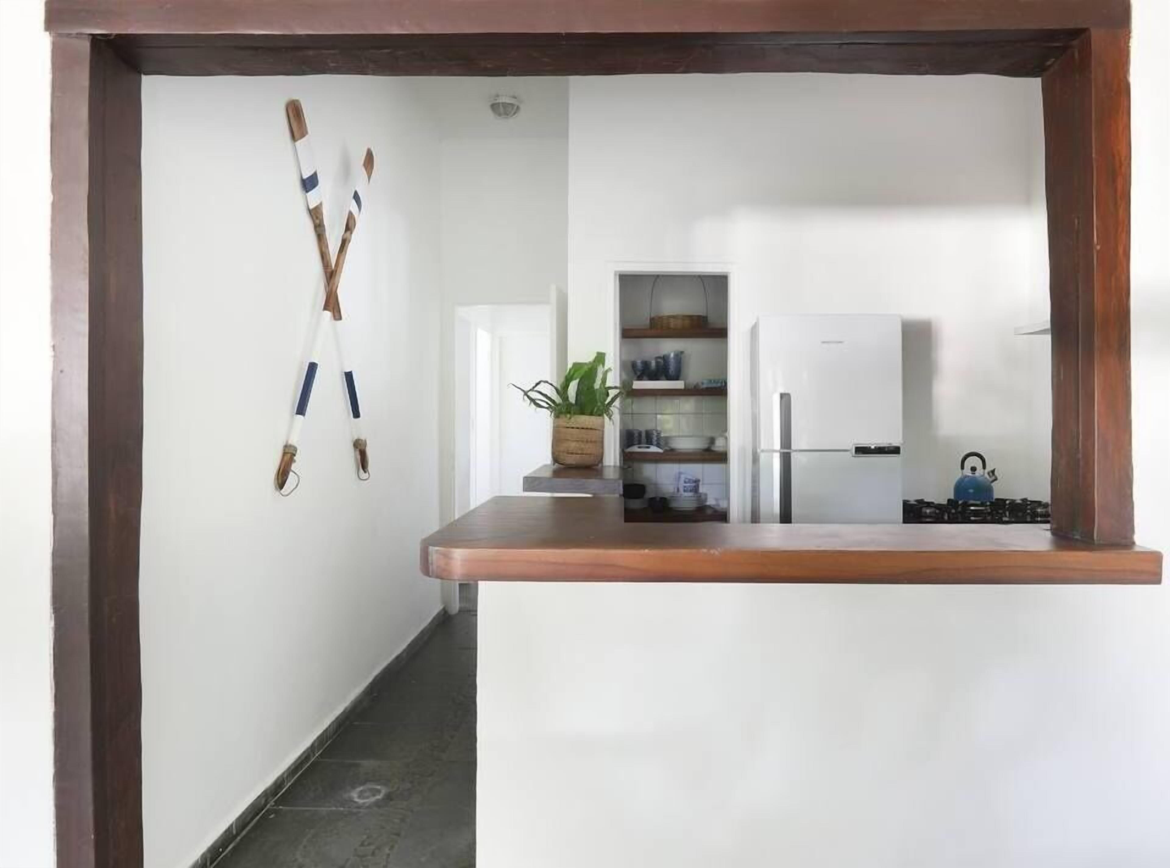 A narrow kitchen with a wooden countertop, a white refrigerator, and a blue kettle on the stove.