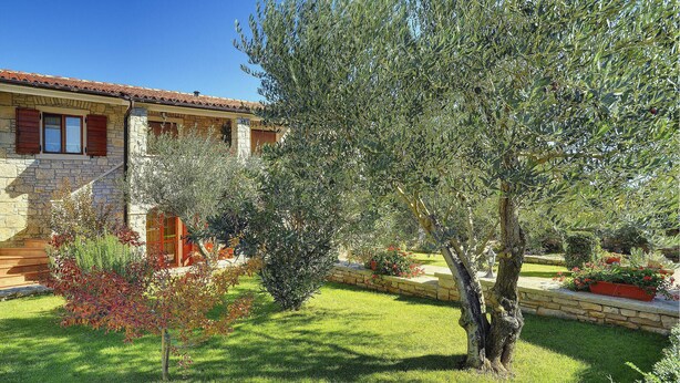 A stone building with a tiled roof and a well-maintained garden with olive trees and shrubs. - 1 bedroom beach front apartment in Rakalj (Rakalj)