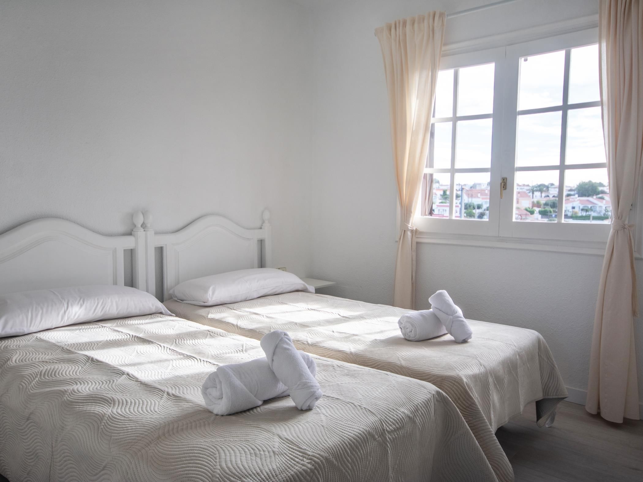 A hotel room with two beds, a window with curtains, and a view of the city.