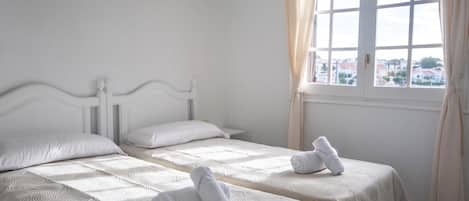 A hotel room with two beds, a window with curtains, and a view of the city.