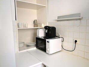 Pieni keittiönurkkaus, jossa on mikroaaltouuni, kahvinkeitin ja pinottuja lautasia.