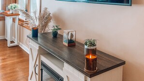A modern living room with a fireplace, a large flat-screen TV mounted on the wall, and a wooden coffee table with decorative items. - Enjoy Lakefront Sunsets in Cozy 2BR Cottage Escape (Plymouth)