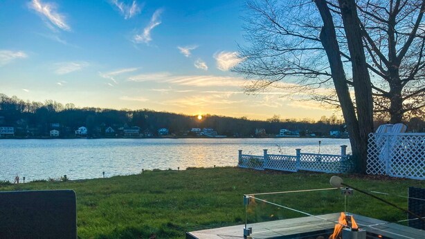 A patio with a fire pit, a view of a lake, and a white fence. - Enjoy Lakefront Sunsets in Cozy 2BR Cottage Escape (Plymouth)