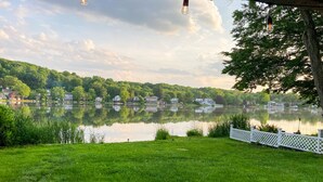 A serene lakeside view with a white fence, calm water, and houses in the background. - Enjoy Lakefront Sunsets in Cozy 2BR Cottage Escape (Plymouth)