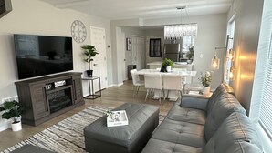 A modern living room with a large sectional sofa, a flat-screen TV, a ceiling fan, and a dining area with a chandelier. - Townhouse on Strand...Centrally located with all new furnishings and Central AC (Missoula)