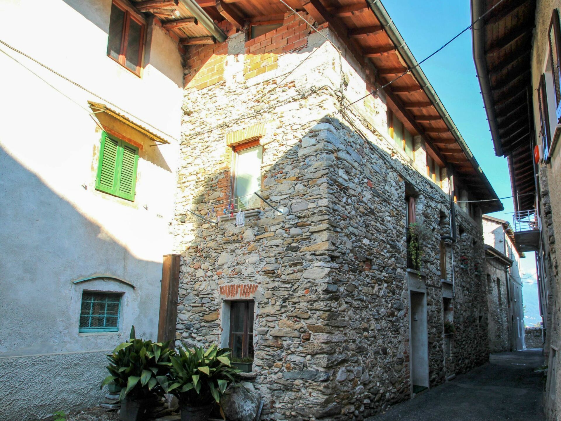 A narrow street with stone buildings, a small shop with a sign, and a potted plant.