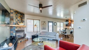 A spacious living room with a fireplace, a red sofa, a glass coffee table, and a dining area with a kitchen in the background.