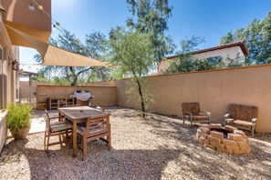 Une terrasse extérieure avec une table et des chaises en bois, un barbecue et un foyer en pierre.