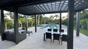 Eine Terrasse im Freien mit Pool, überdachter Sitzgelegenheit und einem Tisch mit Stühlen.