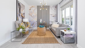 Een moderne woonkamer met een bank, salontafel, bijzettafeltje, lamp en een groot raam.