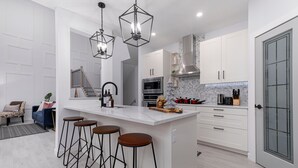 Een moderne keuken met een centraal eiland, een paar barkrukken, roestvrijstalen apparatuur en witte kastjes.