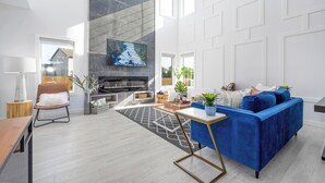 Een moderne woonkamer met een blauwe bank, een open haard en een televisie bevestigd aan een marmeren muur.
