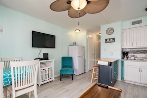 A compact living space with a TV, a teal chair, a white refrigerator, and a kitchenette.