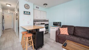 A compact living space with a kitchenette, a dining area with stools, a sofa with a patterned pillow, and a remote control on a side table. - Sunrise Beach Retreat (Corpus Christi)