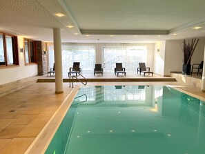 Una piscina con piso de baldosas, una barandilla de vidrio y varias sillas de descanso.