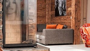 Una sala de estar moderna con una chimenea de piedra, un sofá gris con cojines naranja y un sillón rojo con estampado floral.