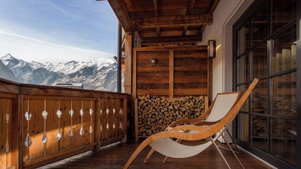 Un balcón de madera con una silla, leña apilada y vistas a la montaña.