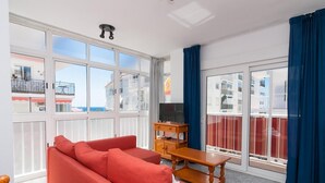 Un moderno salón con un sofá rojo, una mesa de centro de madera y un televisor sobre un mueble bajo. Amplias ventanas ofrecen vistas del paisaje urbano.