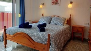 Una cama bien tendida con una colcha estampada, dos lámparas de noche, una mesita de noche de madera y una obra de arte colgada en la pared.