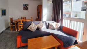Una sala de estar acogedora con un sofá, una mesa de madera y un comedor con sillas y un mueble bajo.