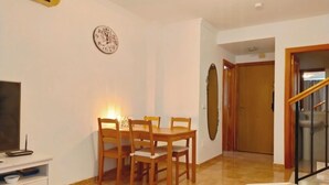 Un coin repas avec une table et des chaises, une horloge au mur et un escalier menant à une autre pièce.