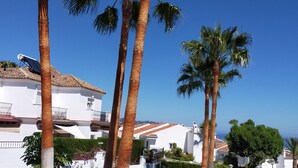 Une villa blanche, dotée d’un toit en tuiles, entourée de palmiers et surplombant un ciel d’un bleu limpide.